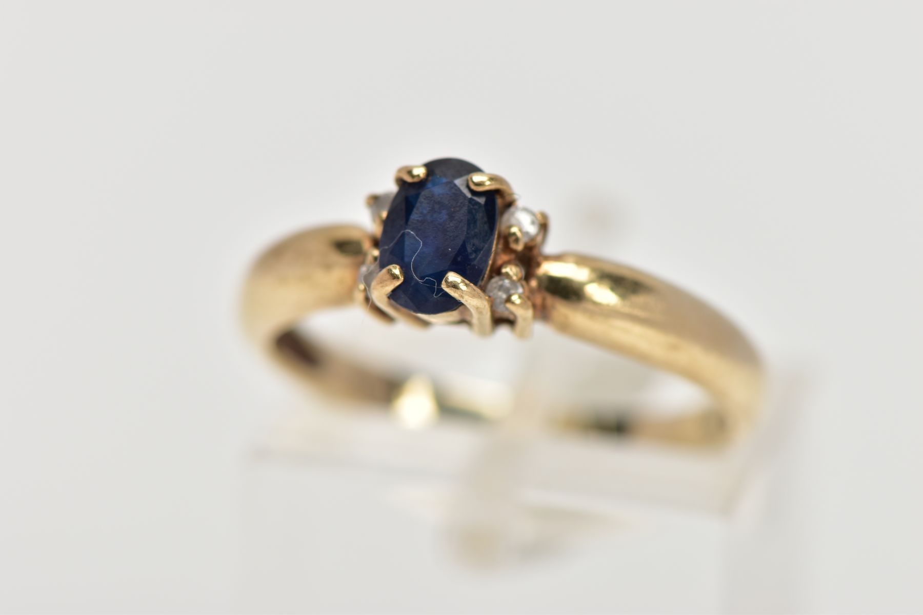 A 9CT GOLD SAPPHIRE AND DIAMOND RING, centring on an oval cut blue sapphire, flanked with four round