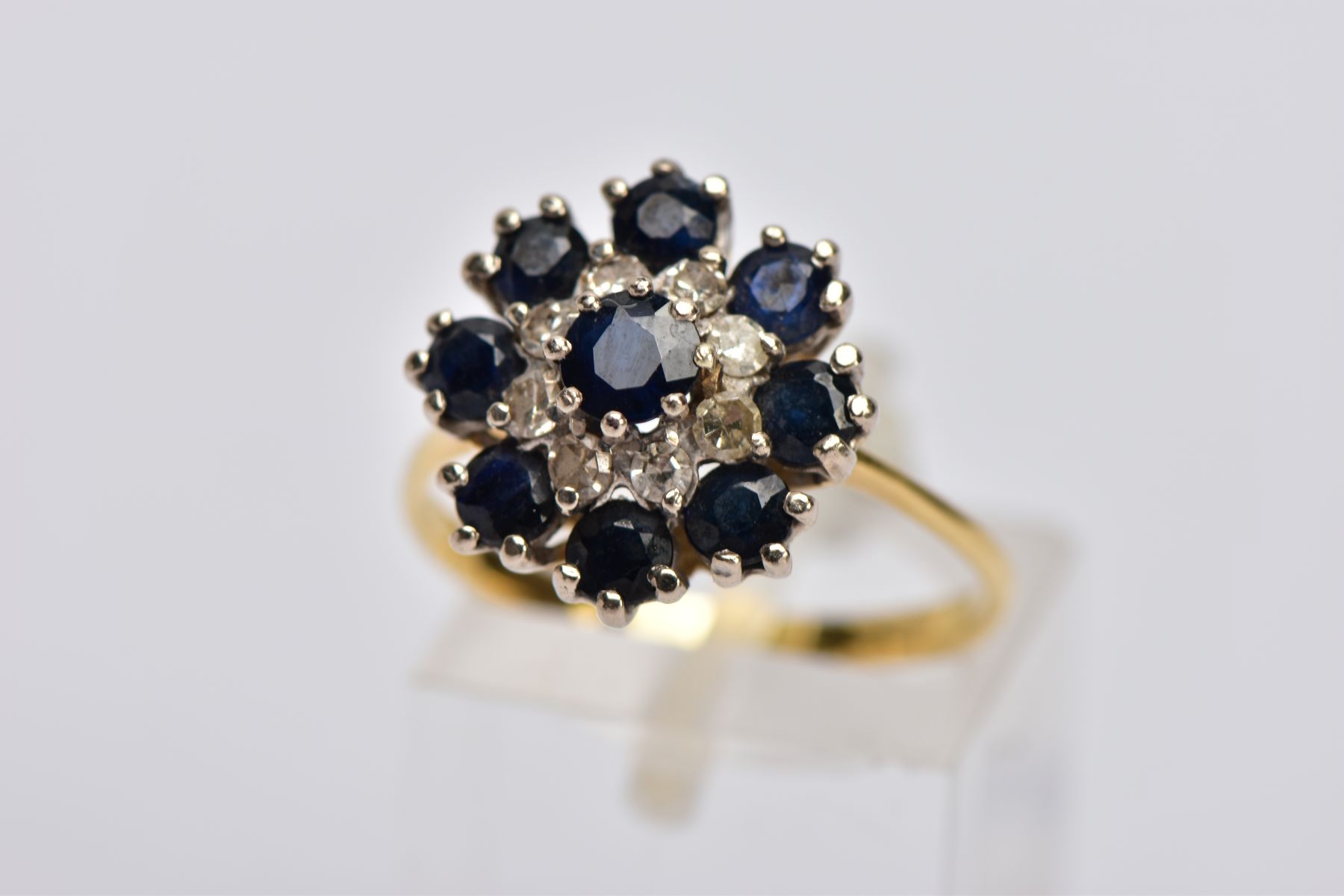 AN 18CT SAPPHIRE AND DIAMOND CLUSTER RING, the central circular sapphire within a tiered single