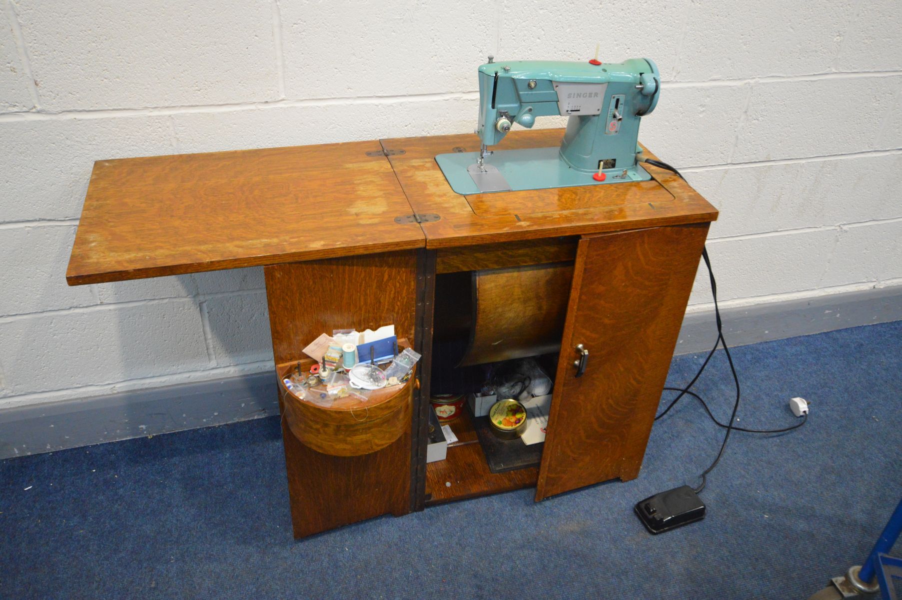 A VINTAGE SINGER SEWING MACHINE in an oak cabinet with sewing accessories (no PAT due to uninsulated