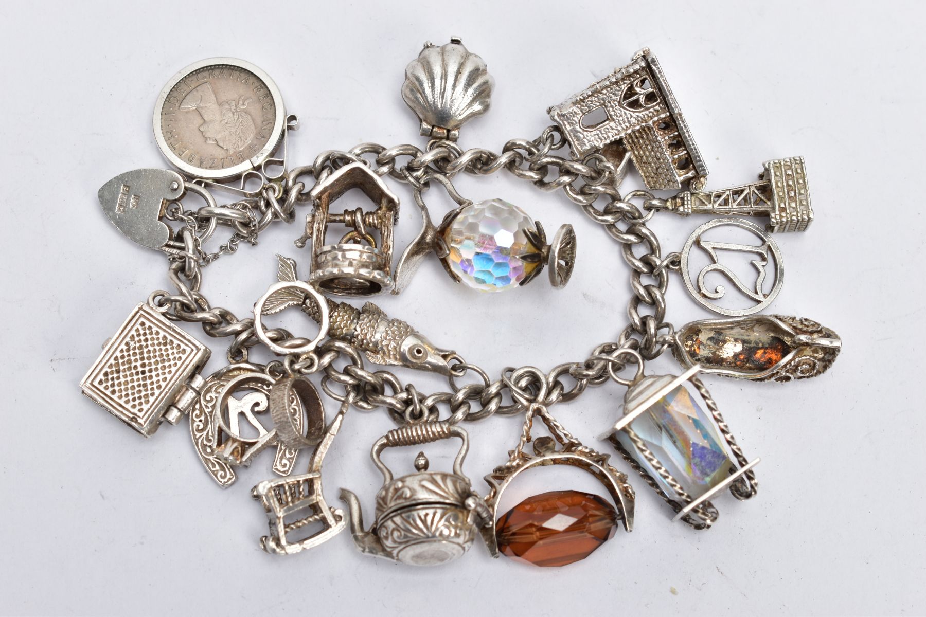 A CHARM BRACELET, the curb link bracelet suspending seventeen charms, to include a hinged shell