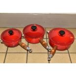 A GRADUATED SET OF THREE LE CREUSET RED ENAMEL SAUCEPANS AND LIDS, wooden handles, diameters 16cm,