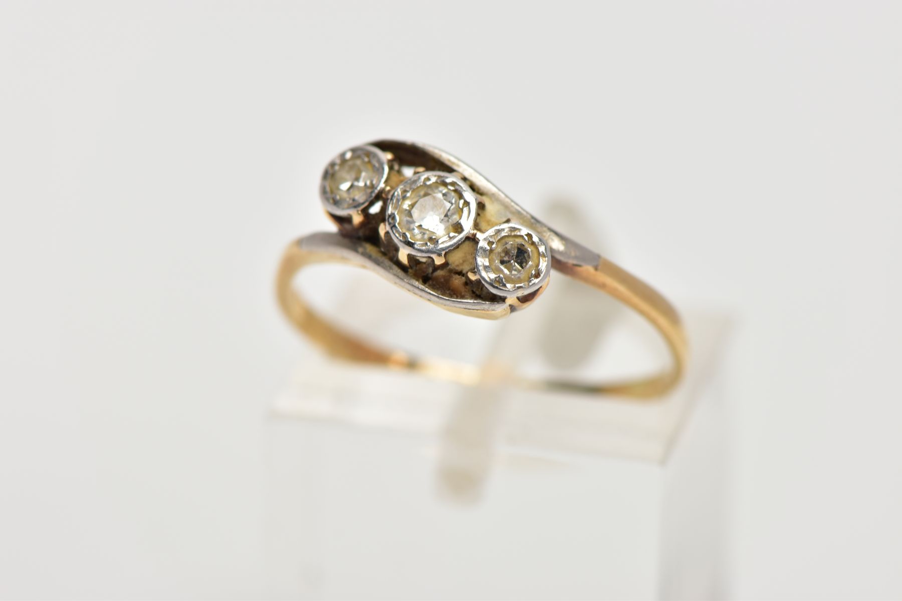 A YELLOW METAL, THREE STONE DIAMOND RING, of a crossover design, set with three illusion set round