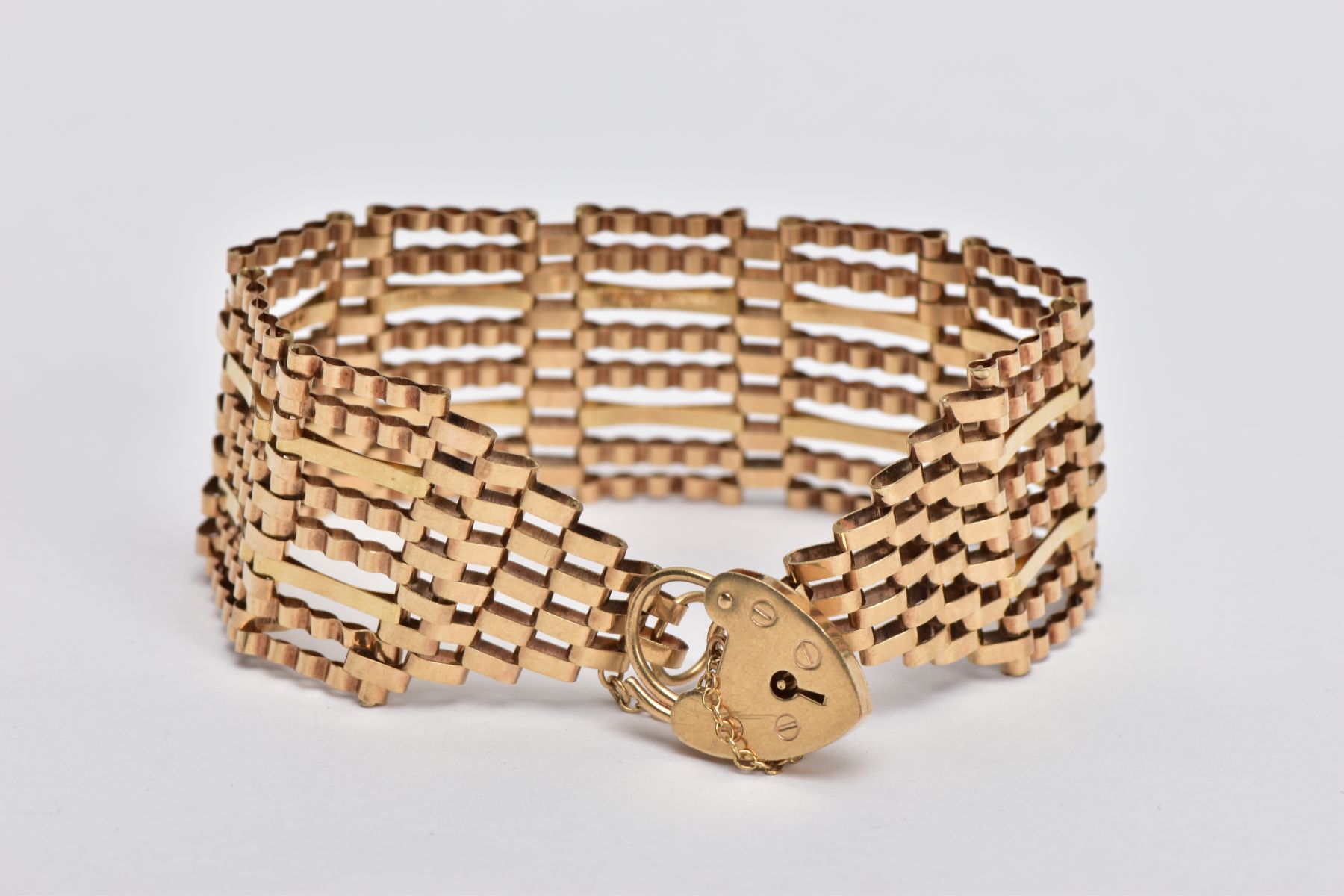 A 9CT GOLD WIDE GATE BRACELET, the gate bracelet with graduated terminals to the heart padlock clasp