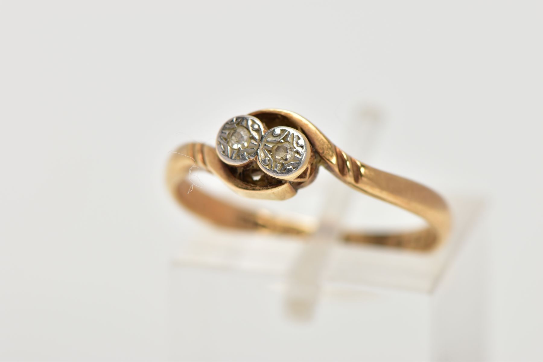 A YELLOW METAL DIAMOND RING, designed with two illusion set, single cut diamonds, crossover