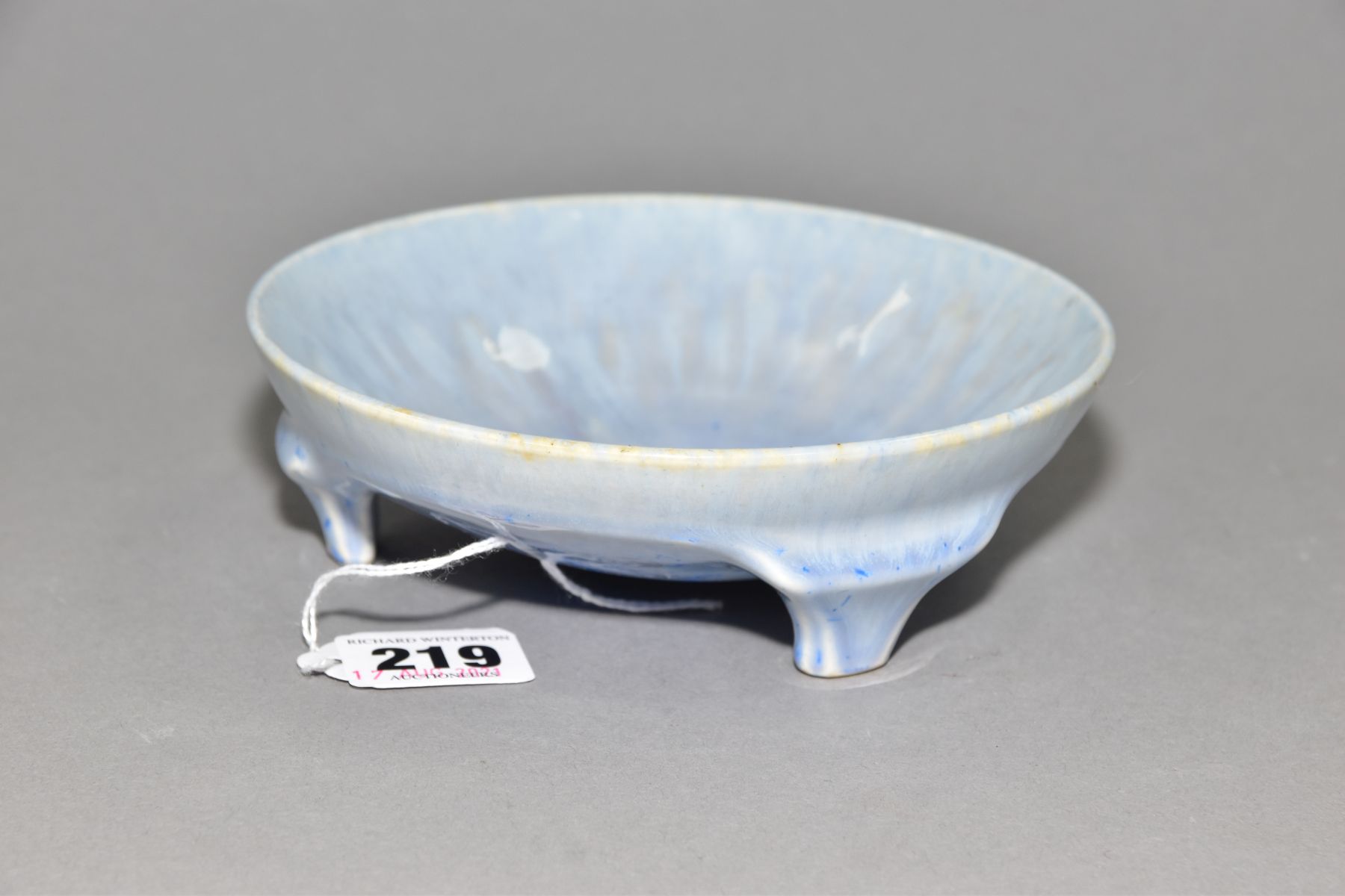 RUSKIN POTTERY, a shallow bowl raised on three feet, blue crystalline and streaked glaze,