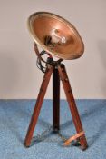 A VINTAGE INDUSTRIAL CONVERTED HEAT LAMP, the light fitting within a coppered shade, on a wooden