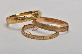 THREE ROLLED GOLD HINGED BANGLES, each decorated with an engraved foliate design, fitted with push