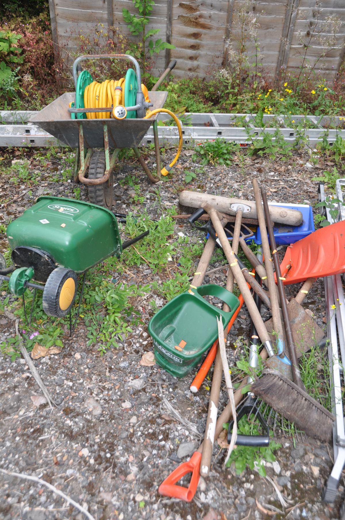 A QUANTITY OF GARDEN TOOLS AND A WHEELBARROW including spades, rakes, seed spreaders, hosepipe on