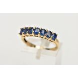 A 9CT GOLD SAPPHIRE DRESS RING, of a half hoop design, set with a row seven claw set, oval cut, blue
