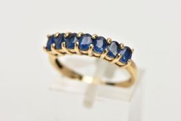 A 9CT GOLD SAPPHIRE DRESS RING, of a half hoop design, set with a row seven claw set, oval cut, blue