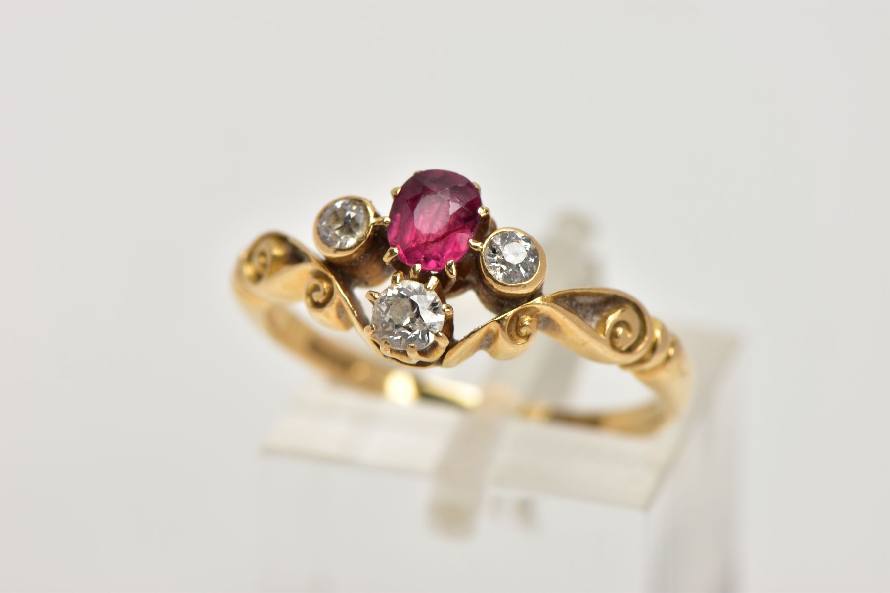 A YELLOW METAL RUBY AND DIAMOND DRESS RING, designed with a cushion cut ruby, flanked with old cut