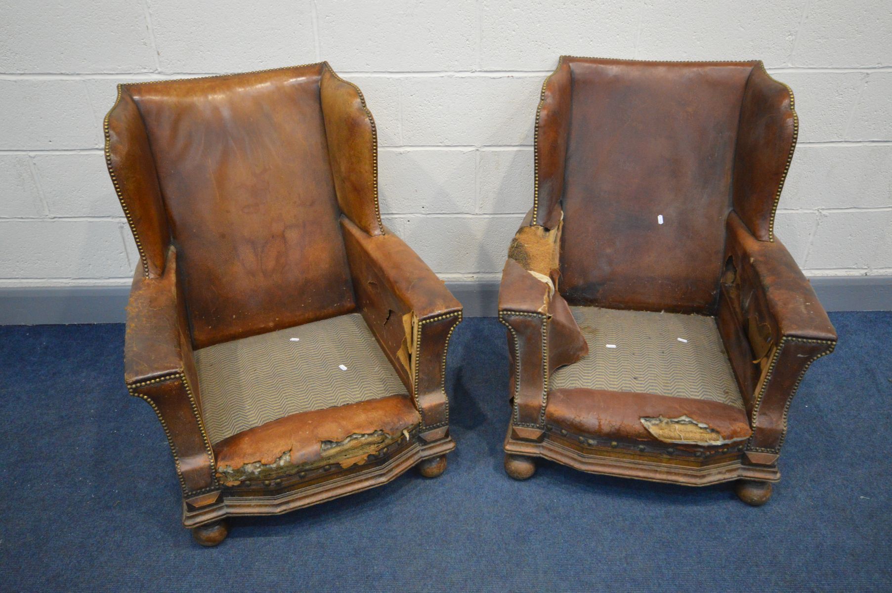A PAIR OF DISTRESSED EARLY 20TH CENTURY BROWN LEATHER WINGBACK CLUB CHAIRS, on front bun feet, width