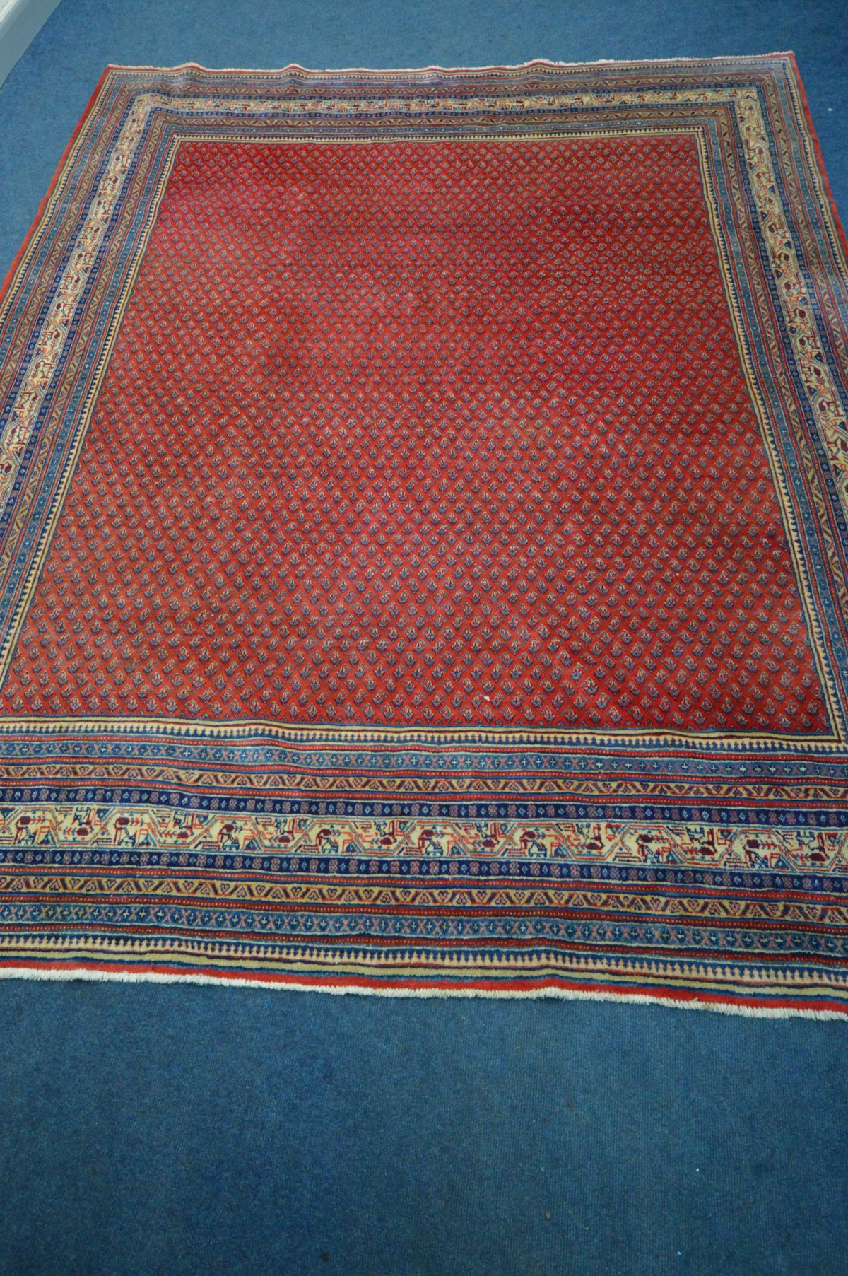 A RED GROUND WOOLEN RUG with a multistrap border, 360cm x 262cm (condition - overall good
