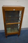 AN EARLY 20TH CENTURY OAK DISPLAY CABINET, the single glazed door enclosing three glass shelves,