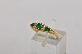 A YELLOW METAL, EMERALD AND DIAMOND RING, designed with a central circular cut emerald, flanked with