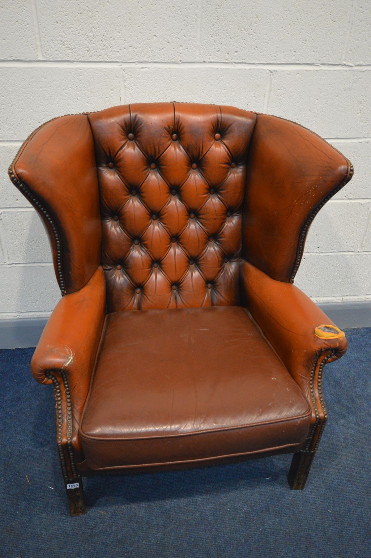 A BURNT ORANGE LEATHER BUTTON WINGBACK ARMCHAIR (condition - rip to left arm, crack to right arm,