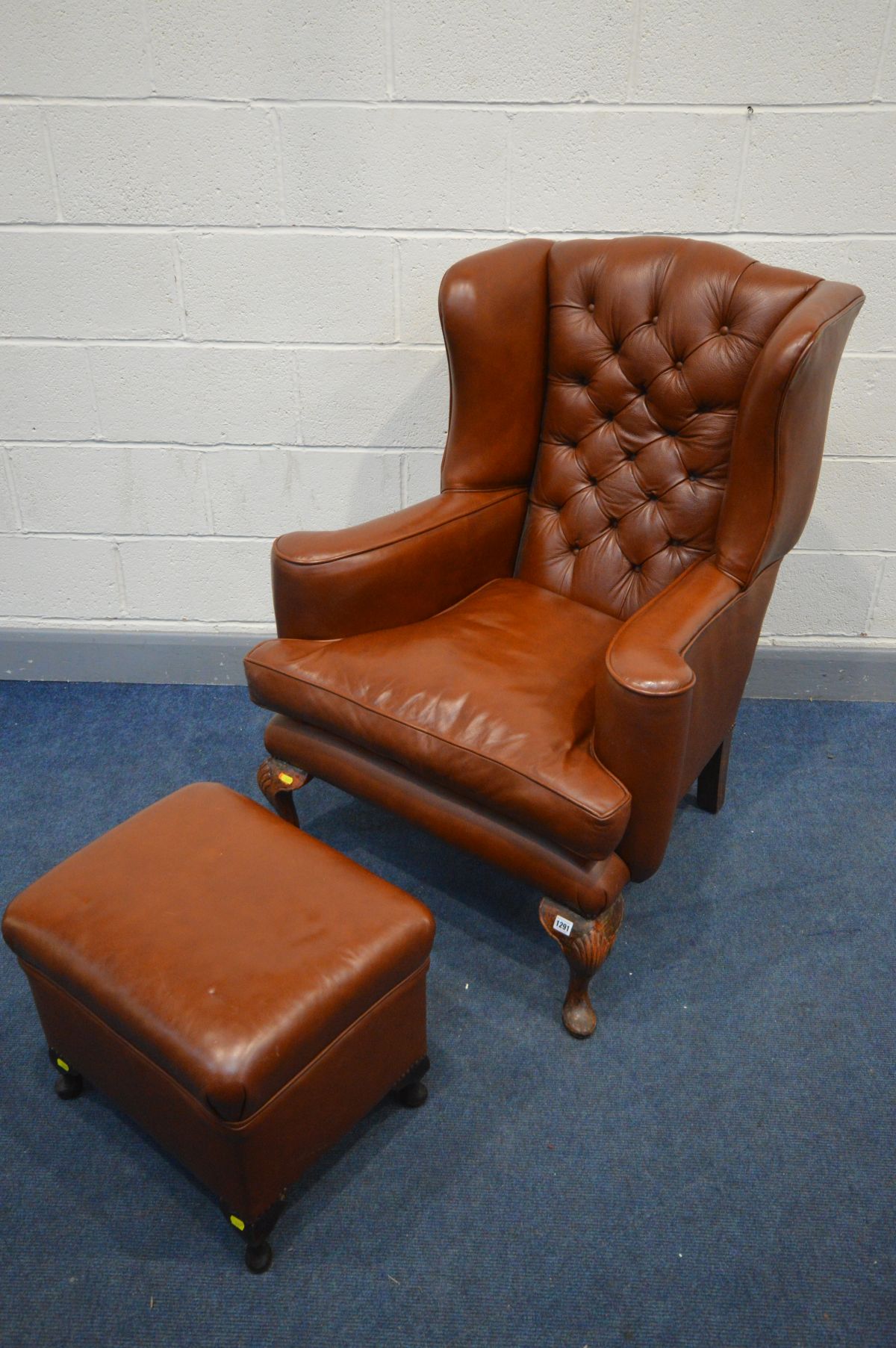 A BROWN LEATHER BUTTONED WING BACK ARMCHAIR, with flat outswept armrests, on cabriole front legs,