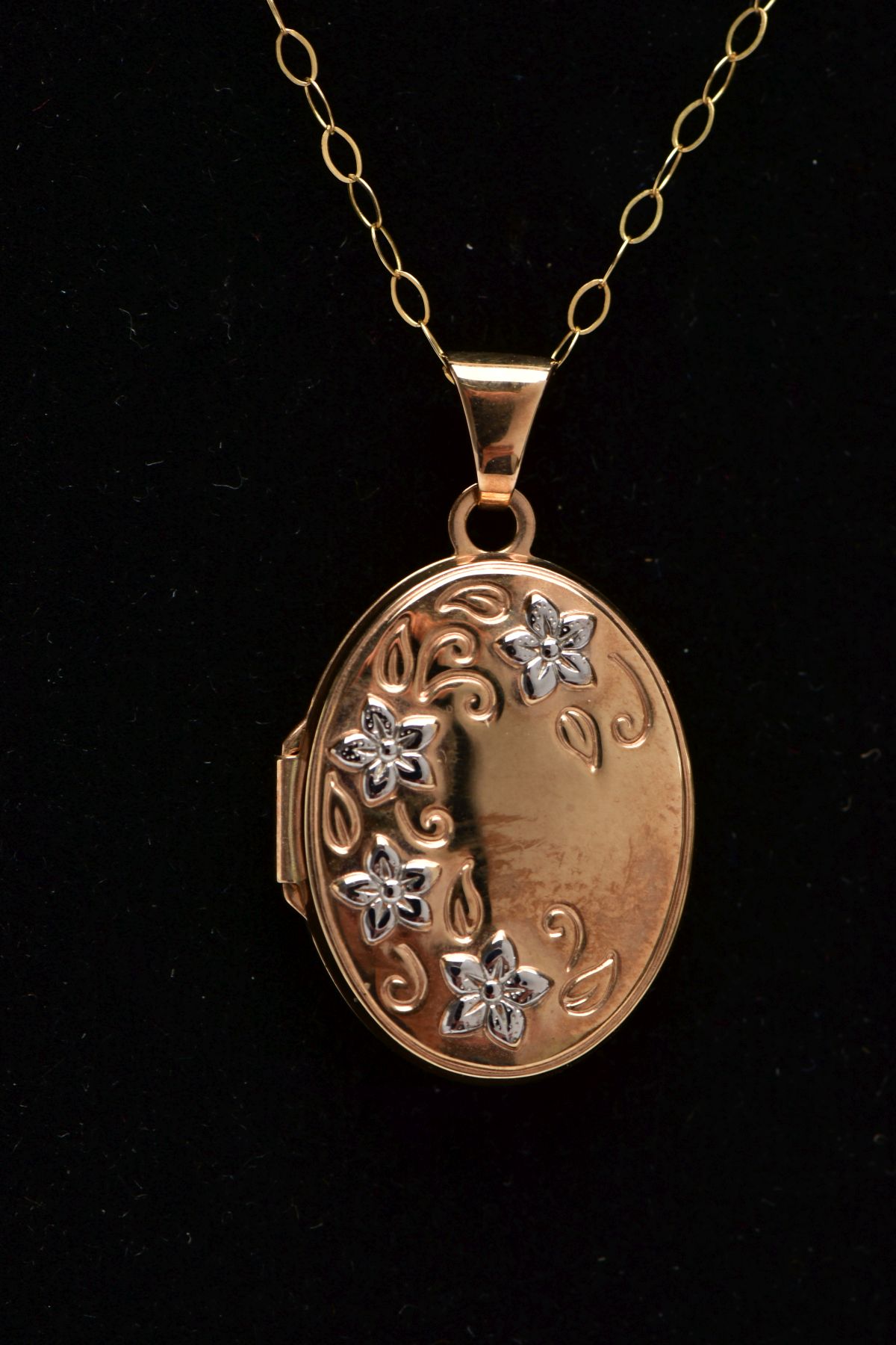 A 9CT GOLD LOCKET PENDANT NECKLACE, the locket of an oval form, decorated with white metal
