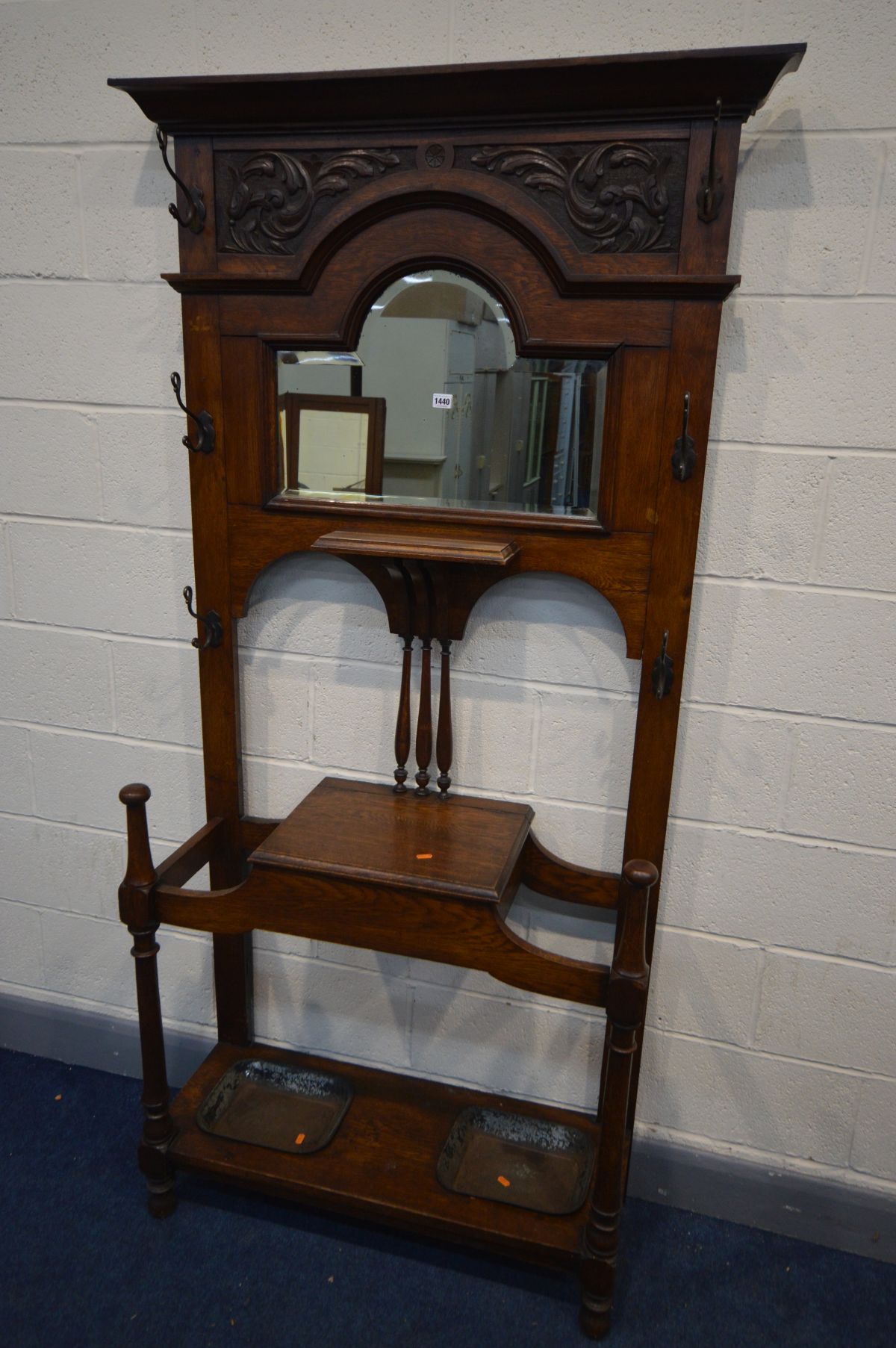 AN EDWARDIAN OAK HALL STAND, with six metal hooks, bevelled edge mirror, hinged storage