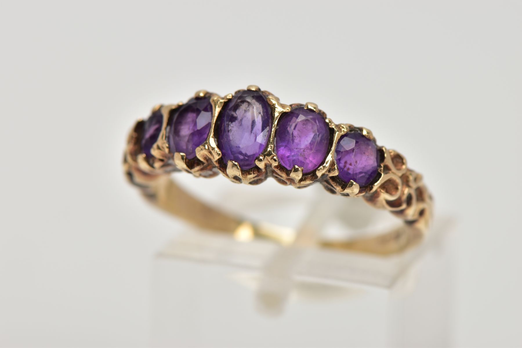 A 9CT GOLD FIVE STONE AMETYHST RING, designed with a row of five graduated oval cut amethyst, scroll