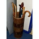 A GROUP OF WALKING STICKS AND UMBRELLAS IN A WICKER STAND, comprising stand, height 70cm, diameter