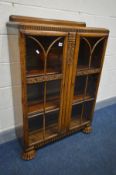 AN ART DECO OAK TWO DOOR BOOKCASE, with three adjustable shelves, on shaped circular front feet,