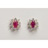 A PAIR OF 9CT GOLD RUBY AND DIAMOND CLUSTER EARRINGS, each designed with an oval cut ruby, within