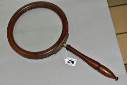 AN OVERSIZED WALNUT FRAMED MAGNIFYING GLASS, moulded circular frame, brass mount with turned screw