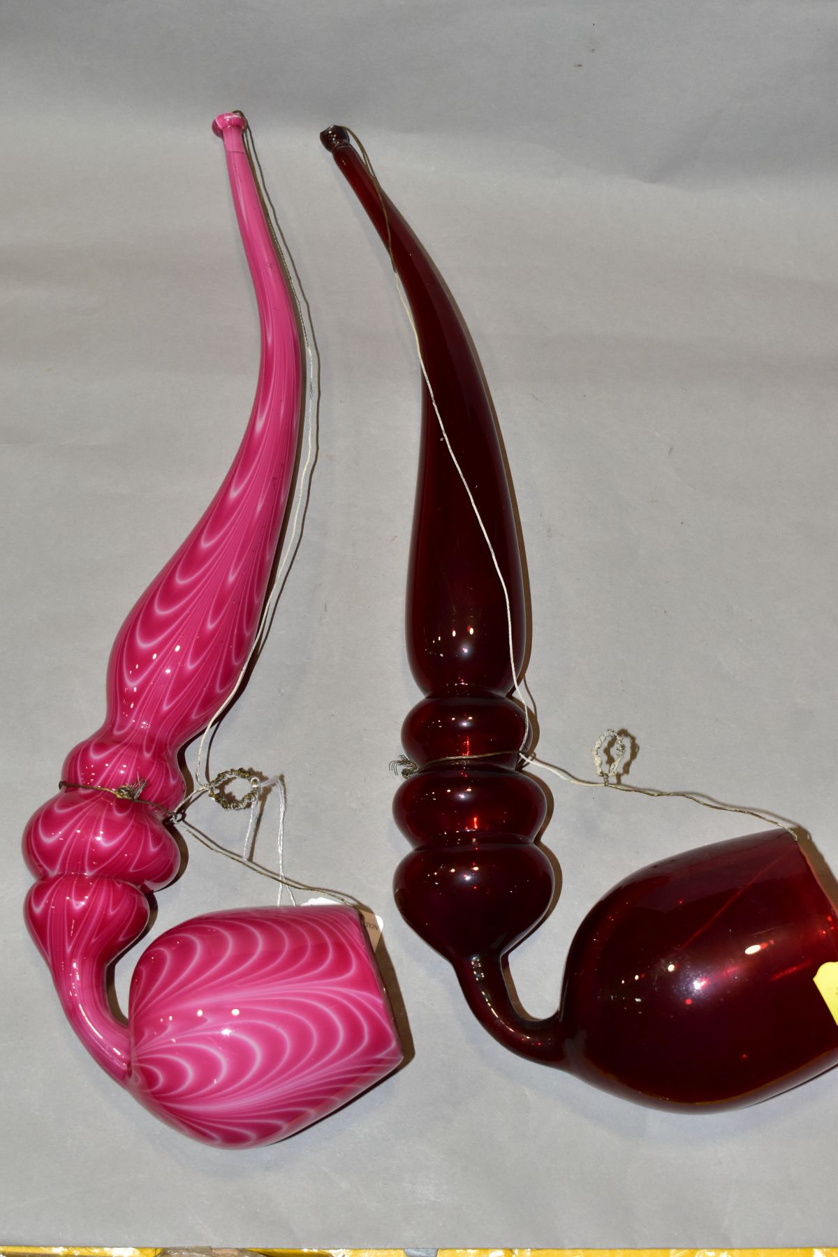 TWO 19TH CENTURY COLOURED GLASS OVERSIZED PIPES, one in ruby glass, the other in opaque pink with