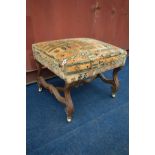 AN EARLY 20TH CENTURY OAK STOOL, on a wavy frame, and later brass casters, width 62cm x depth 56cm x