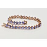 A 9CT GOLD TANZANITE LINE BRACELET, designed with thirty-three claw set, triangular cut tanzanite's,