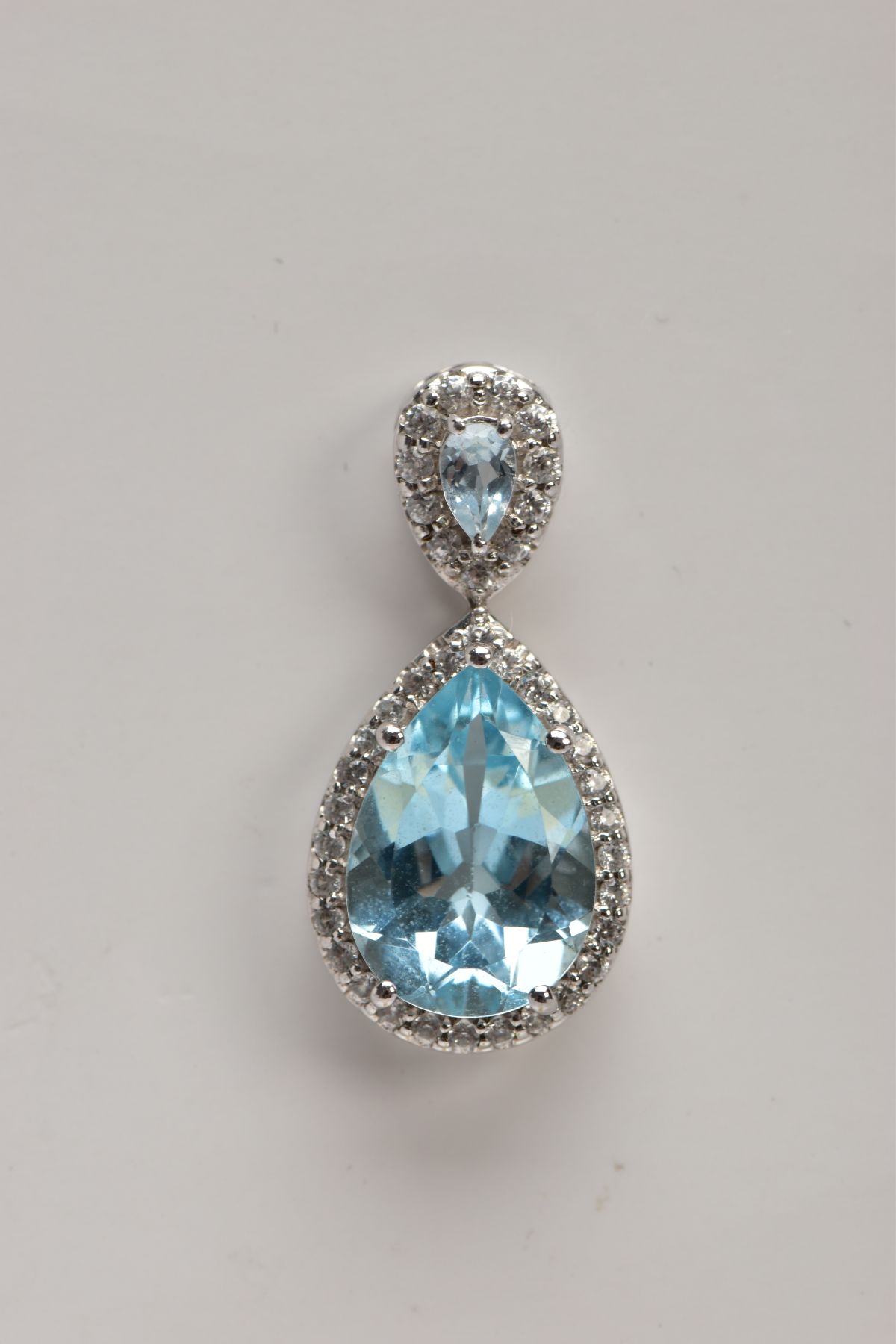 A 9CT WHITE GOLD, BLUE TOPAZ AND SPINEL PENDANT, designed with a pear cut blue topaz, within a