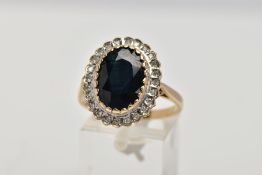A 9CT GOLD SAPPHIRE AND DIAMOND CLUSTER RING, centring on an oval cut deep blue sapphire within a