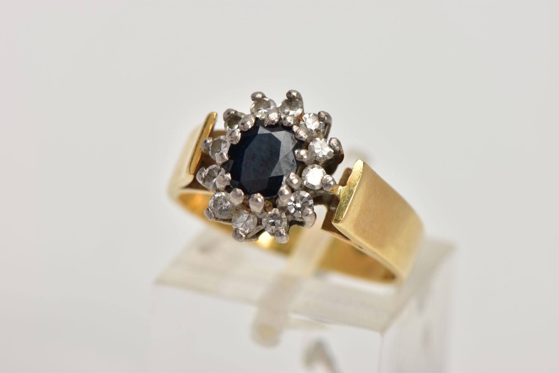 AN 18CT GOLD DIAMOND AND SAPPHIRE CLUSTER RING, centring on an oval cut deep blue sapphire, within a