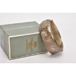 A WIDE SILVER HINGED BANGLE, half of the bangle engraved with a floral and foliate design, push