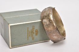 A WIDE SILVER HINGED BANGLE, half of the bangle engraved with a floral and foliate design, push