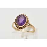 A 9CT GOLD AMETHYST DRESS RING, designed with an oval cut amethyst, collet mount within a rope twist