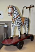 A CHILDS PUSH ALONG WOODEN HORSE, black and white dapple horse on maroon board with black wheels,