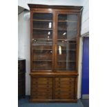AN IMPRESSIVELY TALL VICTORIAN WALNUT BOOKCASE, the overhanging cornice on two large glazed doors,