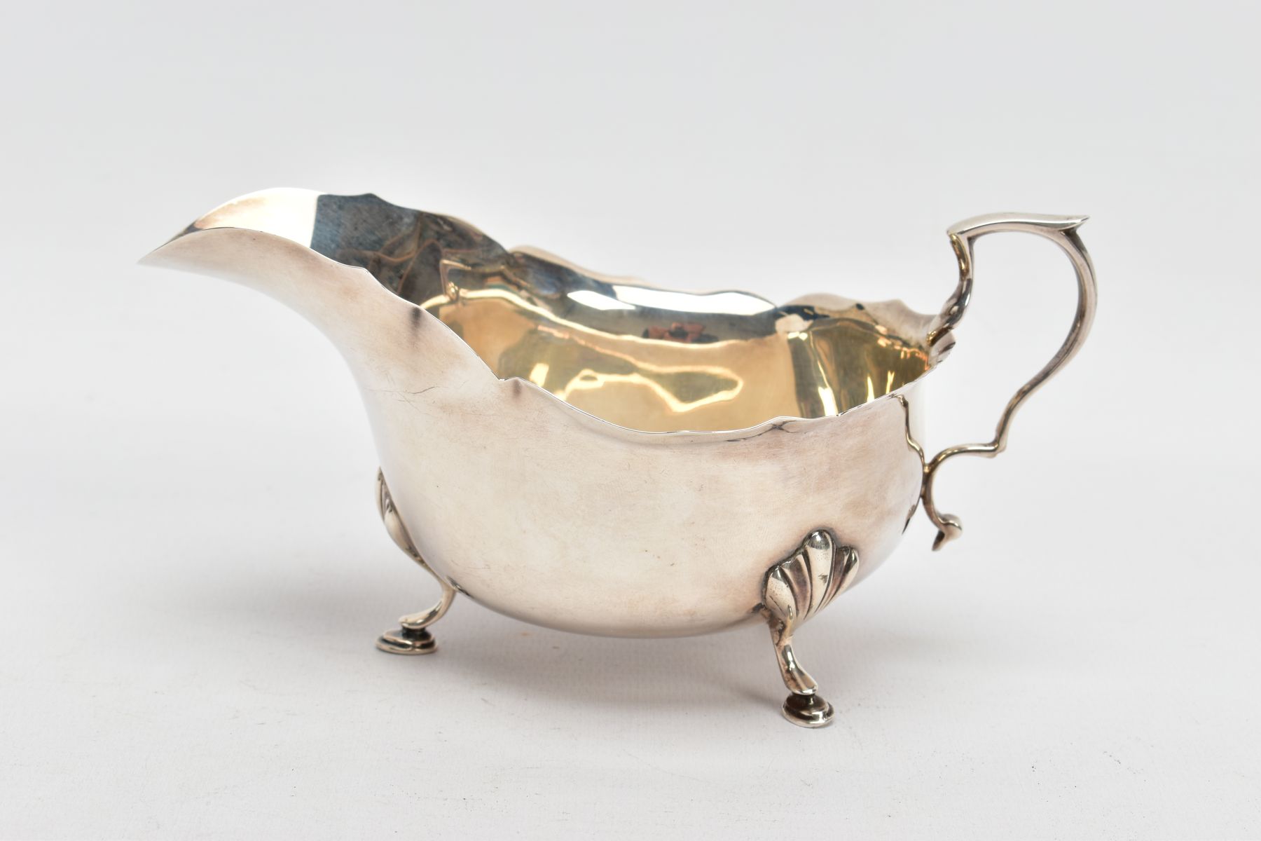 A GEORGE V SILVER GRAVY BOAT, plain polished design, wavy rim, scroll handle, fitted with three hoof