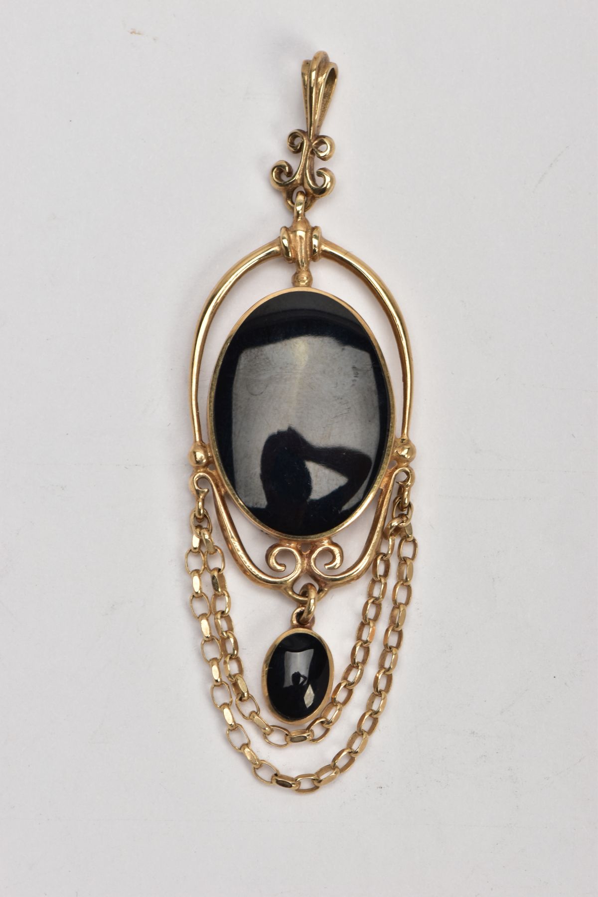 A 9CT GOLD ONYX PENDANT, the oval collet set onyx within a scrolling wire surround suspending a