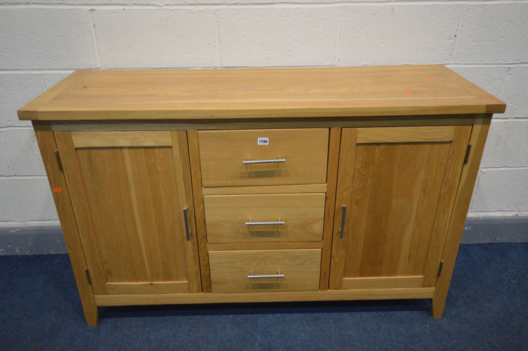 A SOLID OAK SIDEBOARD with two doors flanking three drawers, width 137cm x depth 47cm x 85cm (