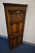 A REPRODUCTION SOLID OAK CORNER CUPBOARD with carved and panelled doors and later shelves, width