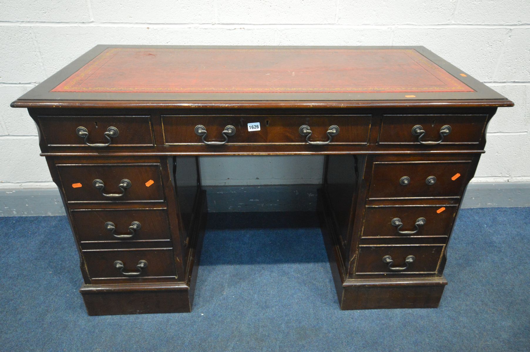 A MAHOGANY PEDESTAL DESK, with oxblood and gilt tooled leather inlayed top and seven assorted