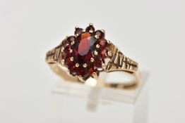 A 9CT GOLD GARNET CLUSTER RING, designed with a central oval cut garnet, within a surround of