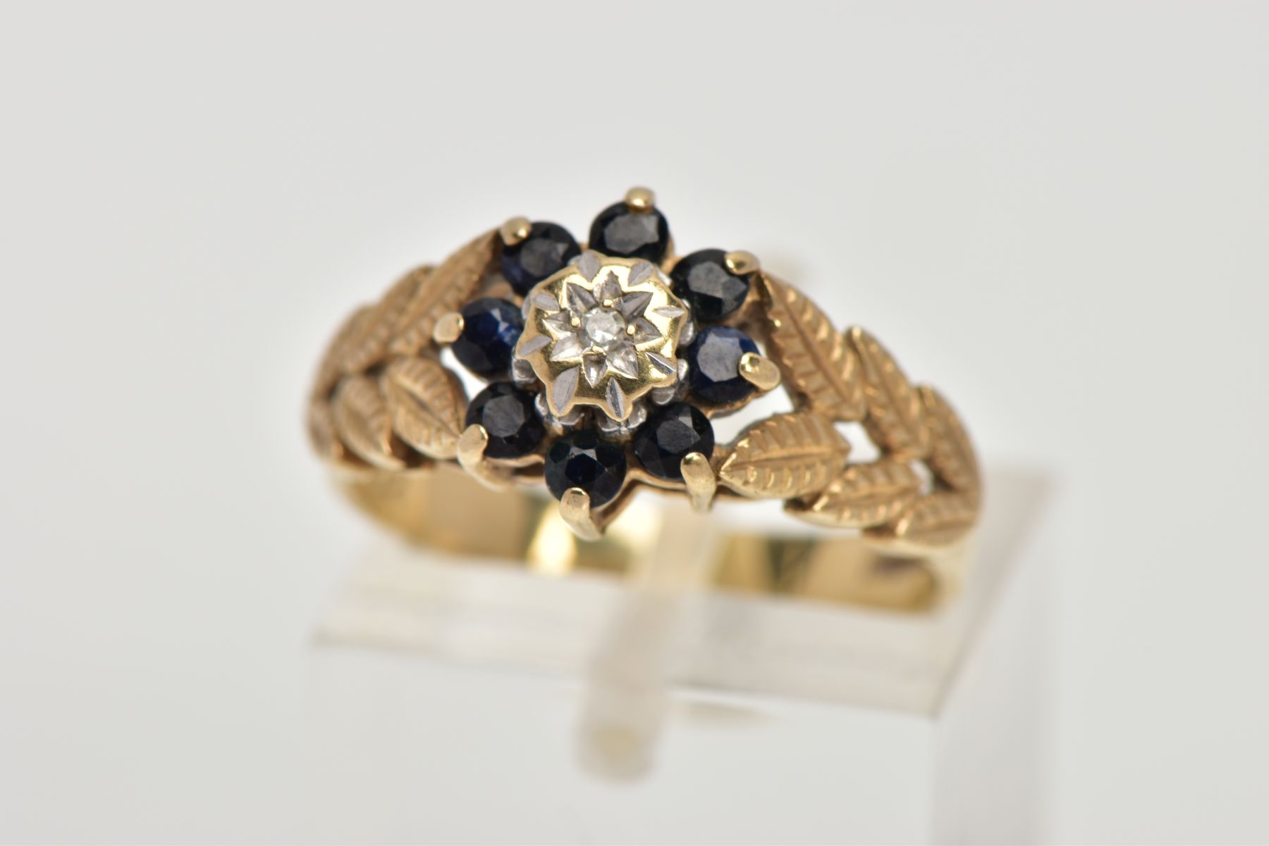 A 9CT GOLD SAPPHIRE AND DIAMOND CLUSTER RING, designed with a star set, single cut diamond, within a
