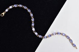 A 9CT GOLD TANZANITE LINE BRACELET, designed with a row of oval cut tanzanite's, fitted with a