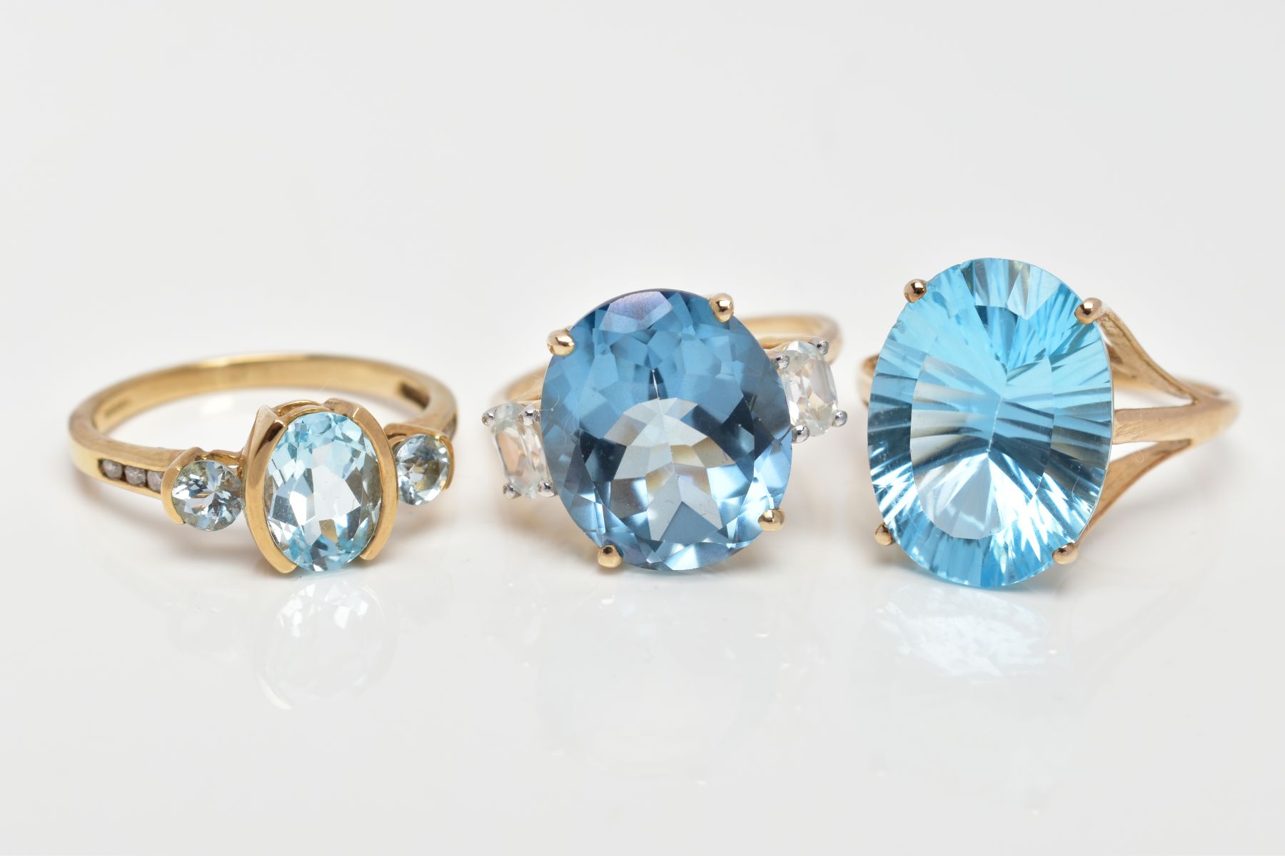 THREE 9CT GOLD DRESS RINGS, the first set with a central oval cut blue topaz, flanked with