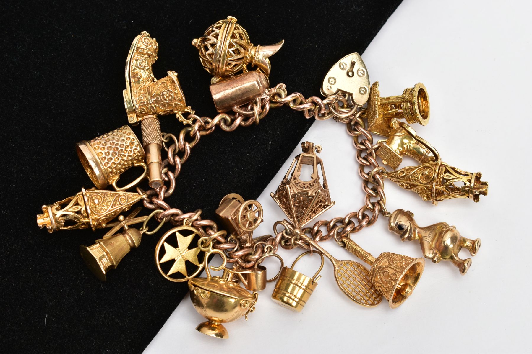 A HEAVY YELLOW METAL CHARM BRACELET, suspending nineteen charms in forms such as a wishing well,