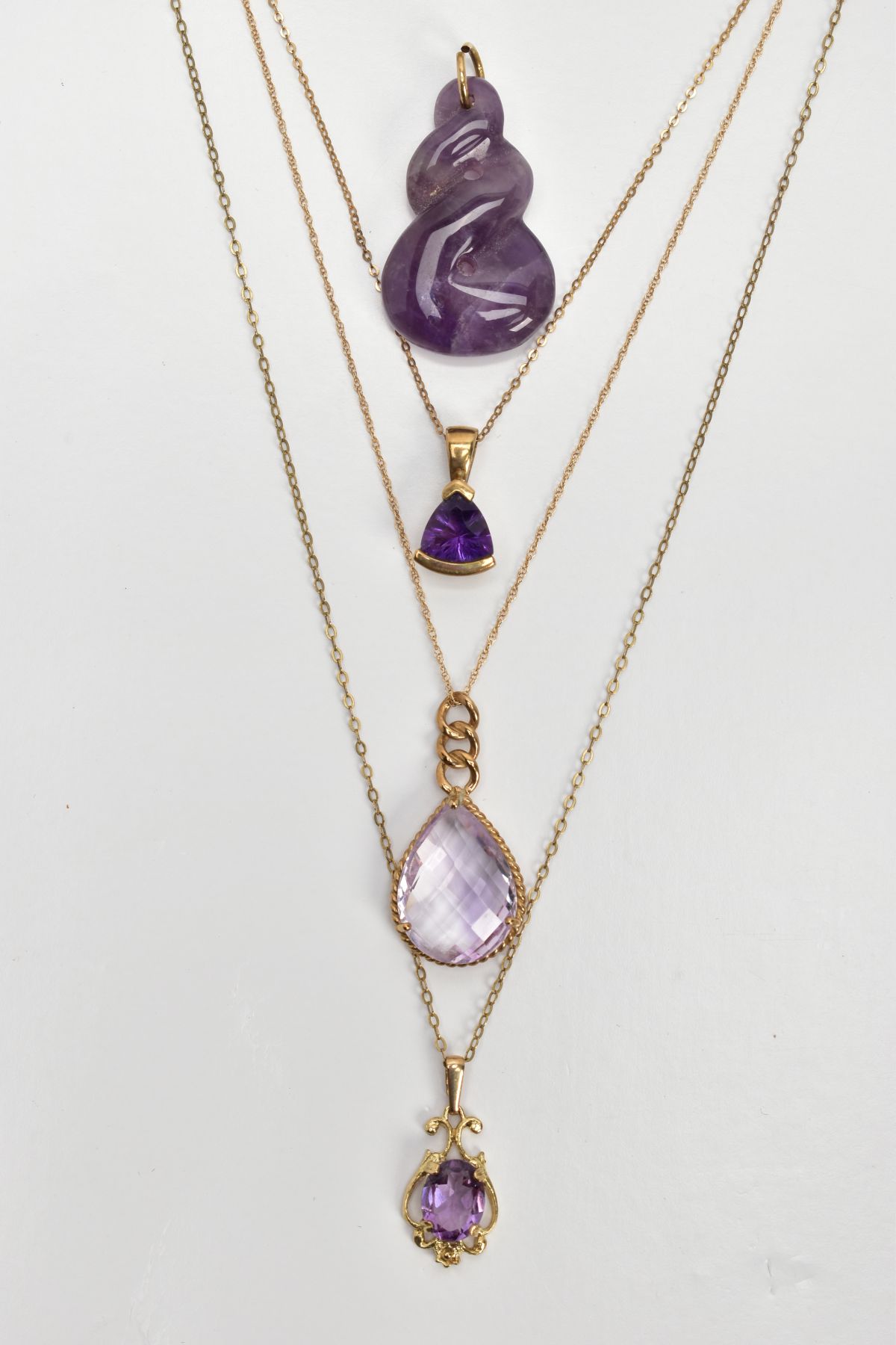 THREE AMETHYST PENDANT NECKLACES AND A CARVED AMETHYST PENDANT, the first a faceted pear cut